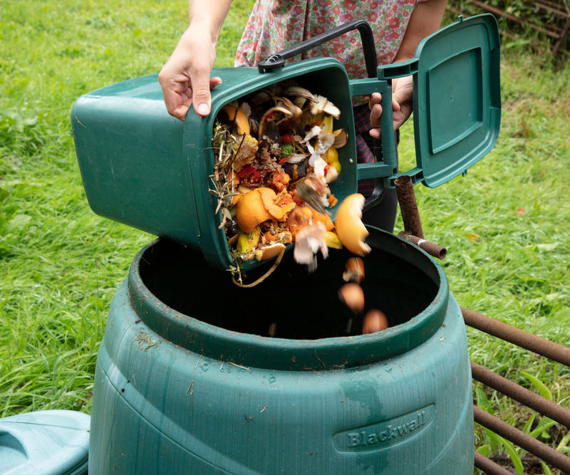 Mujer echando deshechos orgánicos a su compostadora para hacer compostaje doméstico